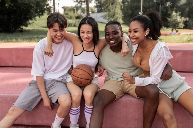 Happy multiracial friends embracing on bench after basketball training